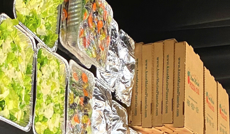 A table covered with catering food like pizza boxes and salads.